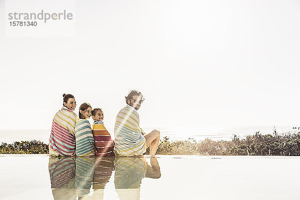 In Handtücher gewickelte Familie sitzt bei Sonnenuntergang am Pool