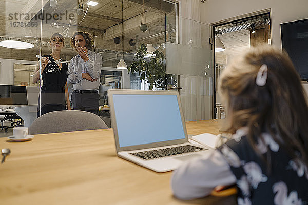 Geschäftsmann und Geschäftsfrau arbeiten an einem Projekt im Büro mit einem Mädchen  das einen Laptop im Vordergrund benutzt