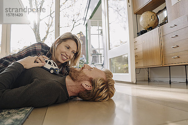 Glückliches Paar liegt zu Hause mit Spielzeugauto auf dem Boden