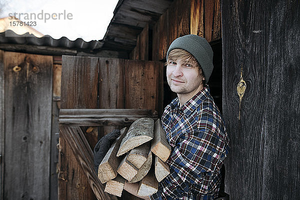 Porträt eines Mannes mit Wollhut  der Brennholz schleppt