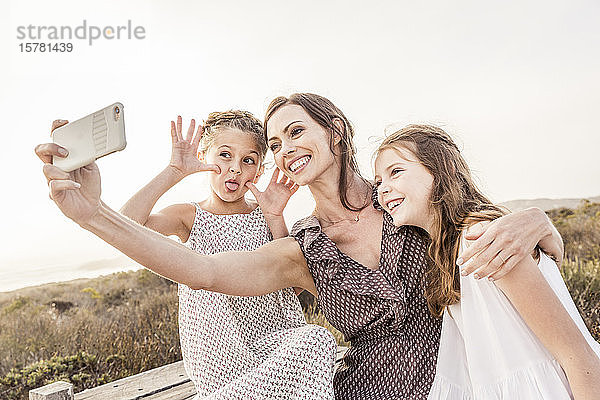 Glückliche Mutter  die mit ihren beiden Töchtern bei Sonnenuntergang auf einer Promenade ein Selfie mitnimmt