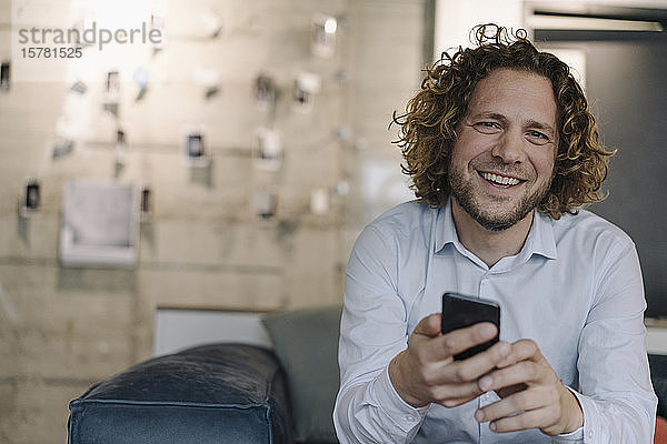 Porträt eines glücklichen Geschäftsmannes mit Handy bei einer Pause im Büro