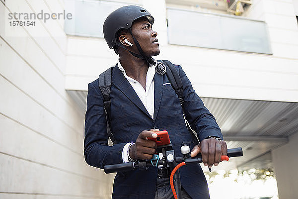 Junger Geschäftsmann mit Roller  Smartphone und Kopfhörern schaut sich um
