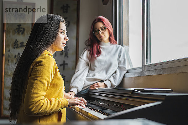 Teenager-Mädchen spielt zu Hause Klavier  während ihre Freundin zuhört