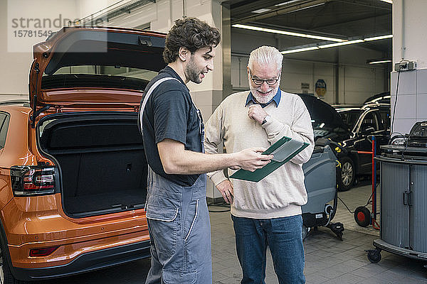 Automechaniker erklärt dem Kunden in der Werkstatt die Checkliste