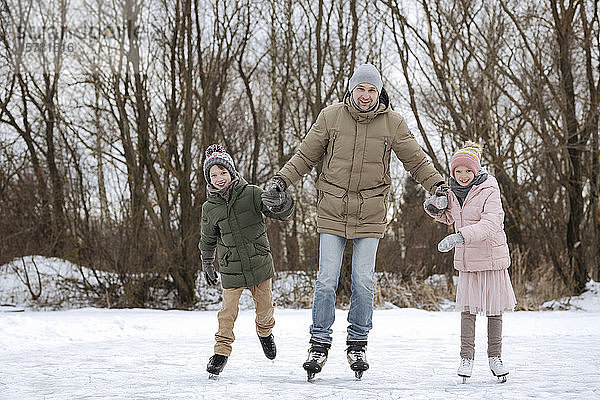 Zwei glückliche Geschwister laufen gemeinsam mit dem Vater auf dem Eis