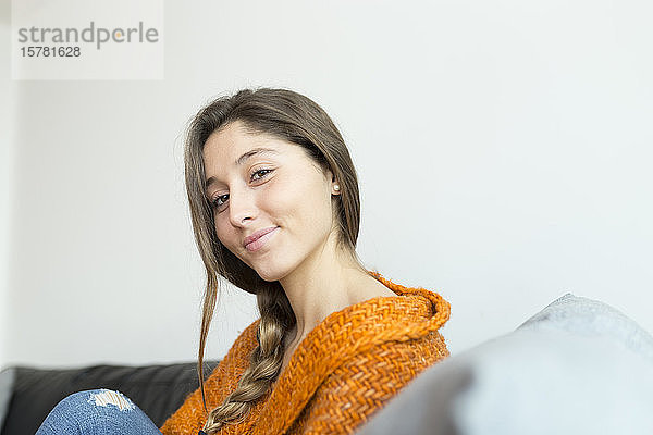 Porträt einer lächelnden jungen Frau mit Zopf  die auf einer Couch sitzt