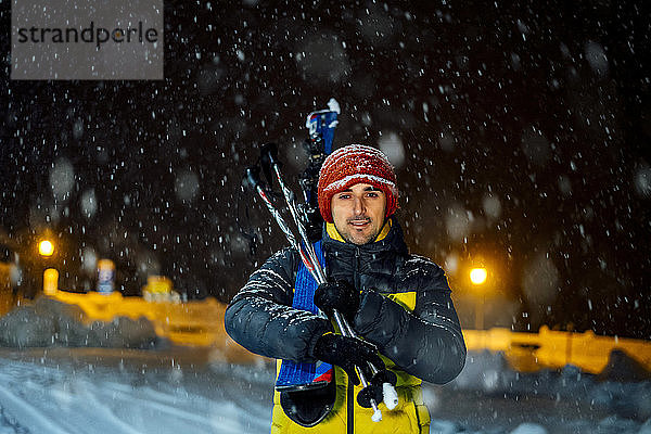 Porträt eines Mannes mit Skiern bei nächtlichem Schneefall