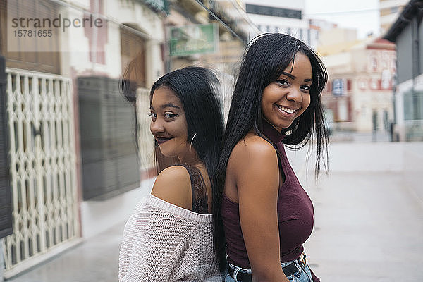 Porträt von zwei glücklichen jungen Frauen  die Rücken an Rücken in der Stadt stehen