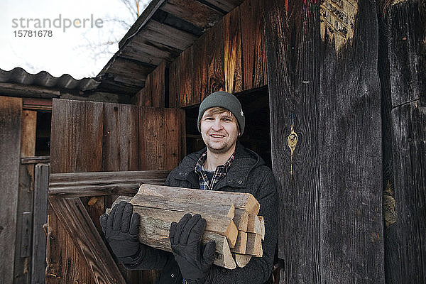 Porträt eines lächelnden Mannes mit Brennholz