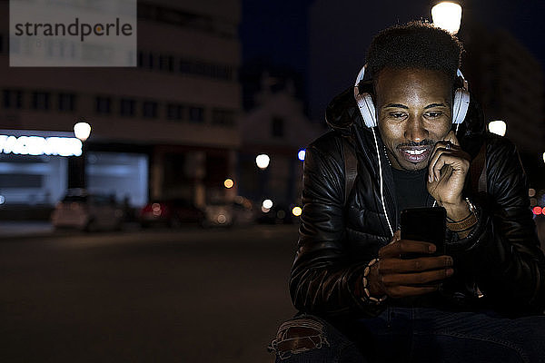 Mann in der Stadt in der Nacht mit Smartphone und Kopfhörern