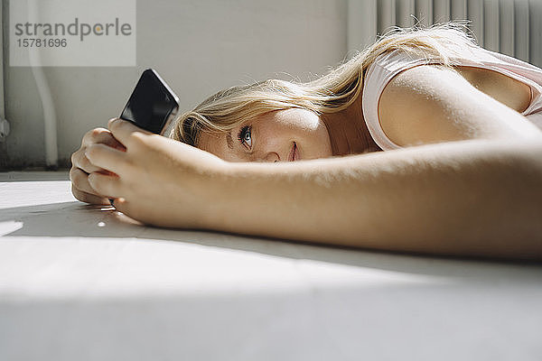 Blonde junge Frau liegt auf dem Boden und benutzt ihr Handy