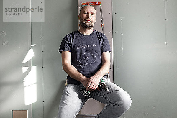 Porträt eines selbstbewussten Mannes  der eine tragbare Bohrmaschine auf einer Baustelle zu Hause hält