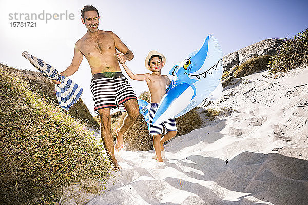 Vater und Sohn mit aufblasbarem Hai auf dem Weg durch die Dünen zum Strand