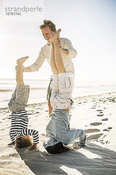 Vater amüsiert sich mit seinem Sohn am Strand  übt Kopfstand