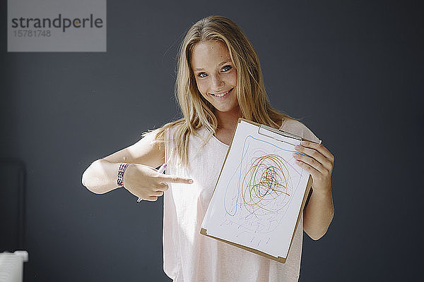 Porträt einer blonden jungen Frau  die mit Gekritzel Papier hält