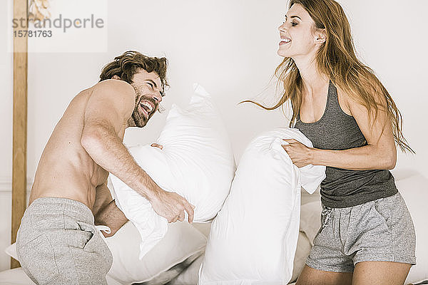 Sorgenfreies junges Paar bei einer Kissenschlacht im Bett