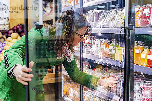 Frau nimmt verpackte Beeren aus dem Kühlregal im Bioladen