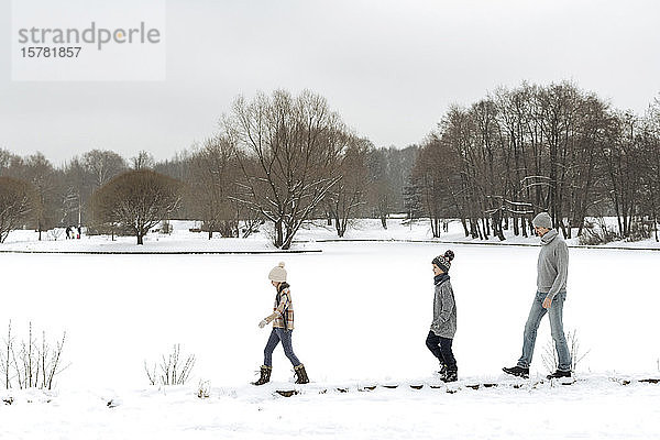Vater und zwei Kinder spazieren in Winterlandschaft