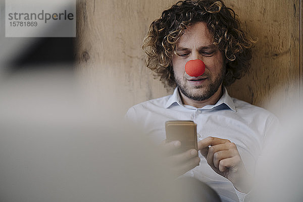 Geschäftsmann mit roter Clownsnase telefoniert im Büro