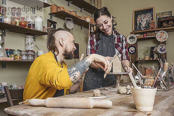 Zwei Töpfer arbeiten gemeinsam an einem kleinen Haus in einer Werkstatt