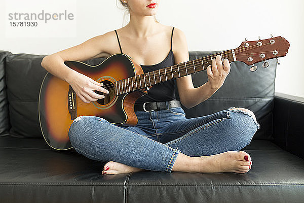 Schrägansicht einer jungen Frau  die auf einer Couch sitzt und Gitarre spielt
