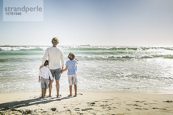 Vater geht mit seinen Söhnen am Strand spazieren und beobachtet das Meer
