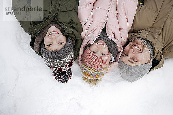 Familienporträt von Vater und zwei Kindern  die auf Schnee liegen
