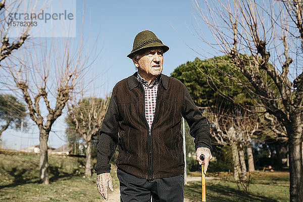 Alter Mann  der im Winterpark spazieren geht und sich auf seine Akne stützt