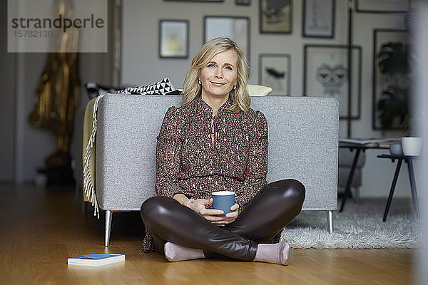 Blonde Frau entspannt zu Hause auf dem Boden sitzend