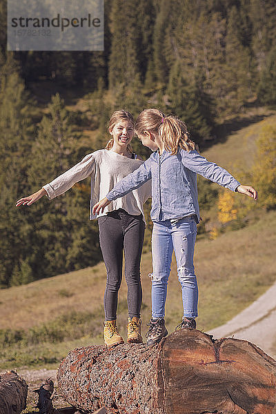 Zwei junge Mädchen balancieren auf einem Baumstamm