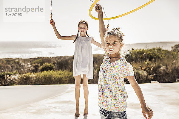 Zwei fröhliche Mädchen spielen mit Springseil und Hoola-Hoop-Reifen auf der Terrasse eines Strandhauses