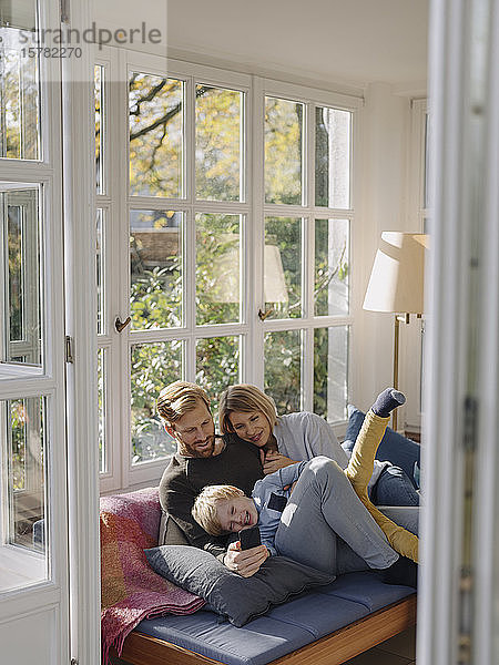 Glückliche Familie benutzt Mobiltelefon im Wintergarten zu Hause