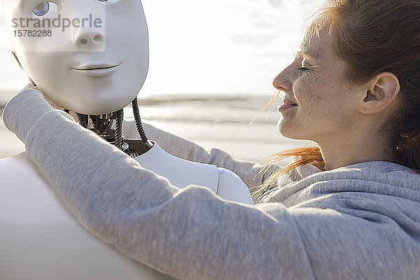 Glückliche Frau umarmt Roboter am Strand