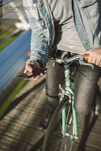 Junger Mann  der mit seinem Fixie-Rad durch die Stadt pendelt und ein Smartphone benutzt