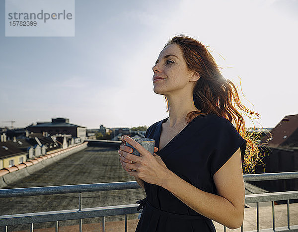 Lächelnde rothaarige Frau bei einer Kaffeepause auf der Dachterrasse