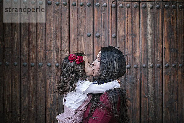 Mutter hält und küsst kleine Tochter im Freien