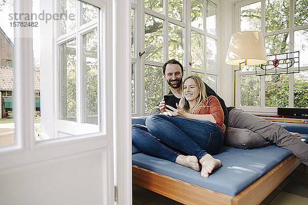 Glückliches Paar entspannt sich auf der Couch  mit Smartphone