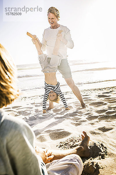 Vater amüsiert sich mit seinem Sohn am Strand  übt Handstand