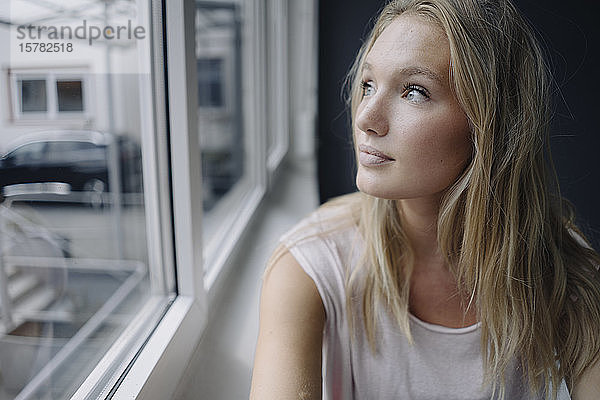 Porträt einer blonden jungen Frau  die aus dem Fenster schaut