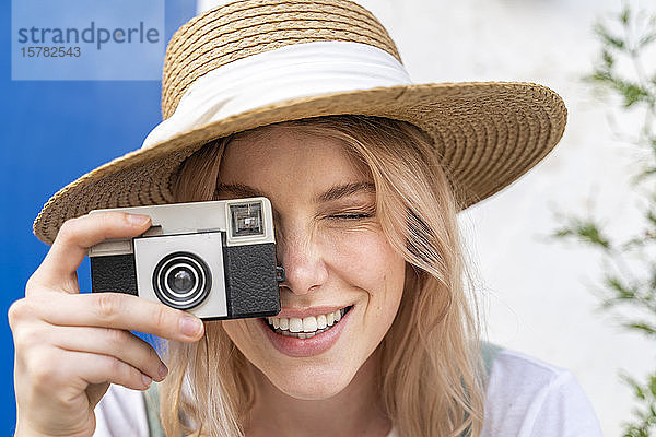 Porträt einer lächelnden jungen Frau mit Strohhut beim Fotografieren mit der Kamera