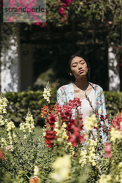 Schöne junge Frau umgeben von Blumen in einem öffentlichen Garten im Frühling