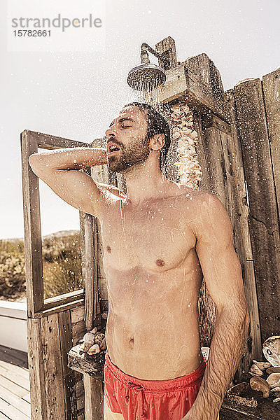 Junger Mann duscht in einer Außendusche