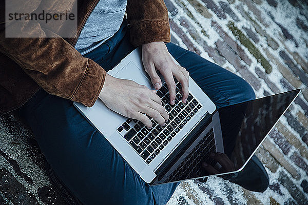 Teenager  der einen Laptop benutzt und auf einem Steinboden sitzt