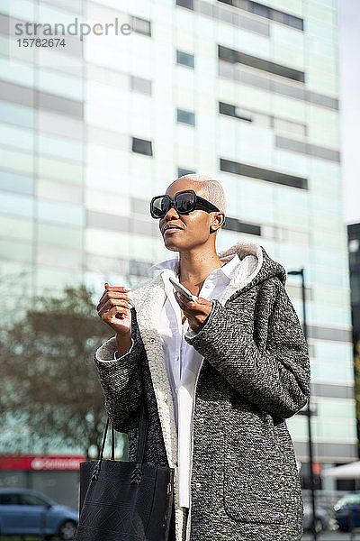 Stilvolle Geschäftsfrau  die in der Stadt pendelt und ein Smartphone in der Hand hält