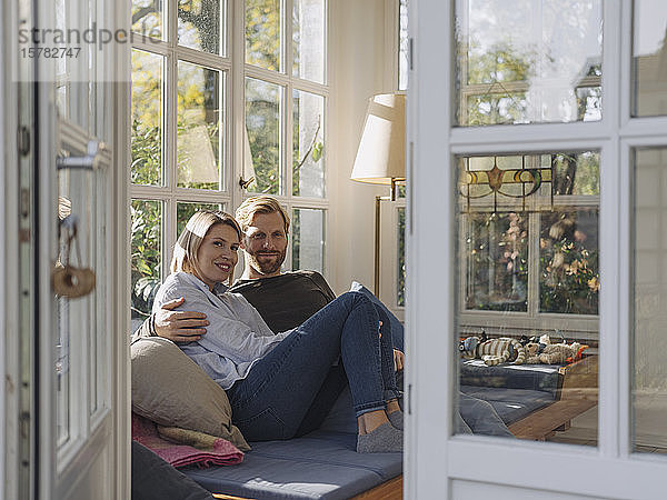 Porträt eines lächelnden Paares  das sich zu Hause im Wintergarten entspannt