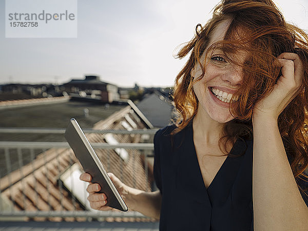 Porträt einer glücklichen rothaarigen Frau mit Tablette auf der Dachterrasse