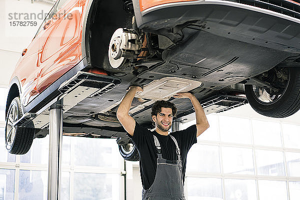 Porträt eines Automechanikers in einer Werkstatt  der vorgibt  ein Auto hochzuheben