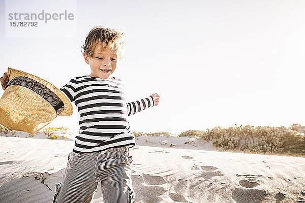 Glücklicher Junge mit Hut läuft am Strand