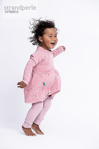 Porträt eines barfüssigen kleinen Mädchens in rosa gekleidet  das vor weissem Hintergrund hüpft